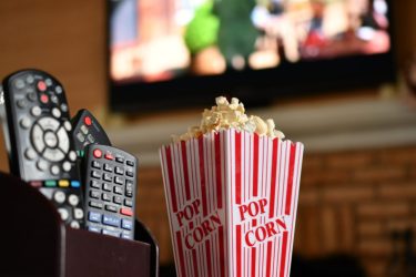 tv-remotes-and-a-container-of-popcorn-with-a-blurred-large-screen-television-mounted-on-wall.jpg